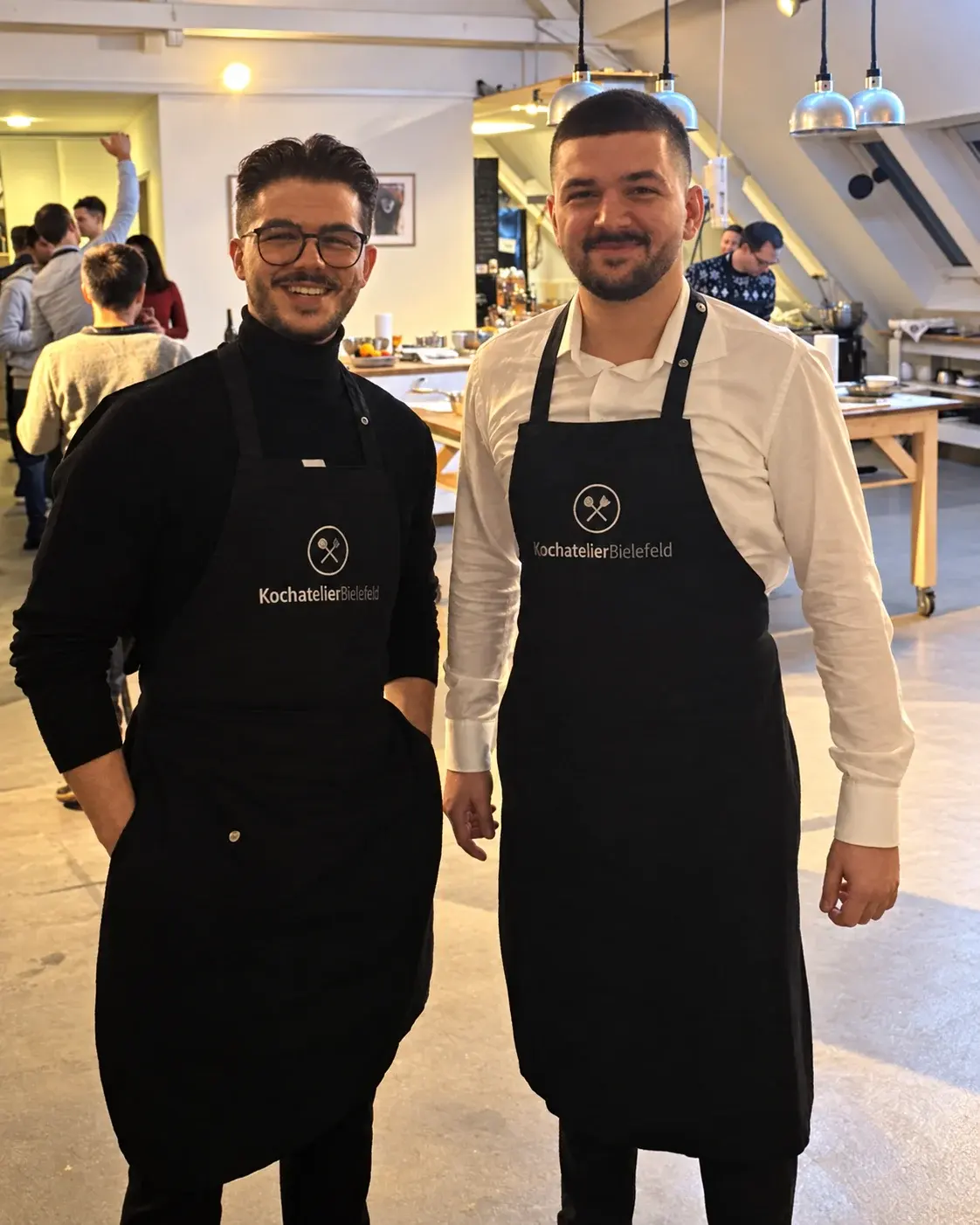 Dion and Rron together at a cooking event, wearing aprons